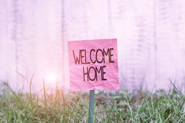 Écriture conceptuelle montrant Bienvenue à la maison. Texte de la photo d'affaires une réception célèbre généralement le retour à la maison d'un papier ordinaire démonstratif attaché au bâton et placé dans la terre herbeuse . — Photo