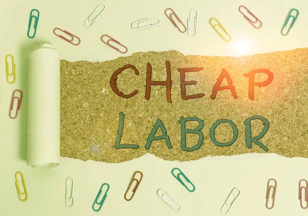 Handwriting text Cheap Labor. Concept meaning when a demonstrating works hard in bad conditions and very little money Paper clip and torn cardboard placed above a wooden classic table backdrop.