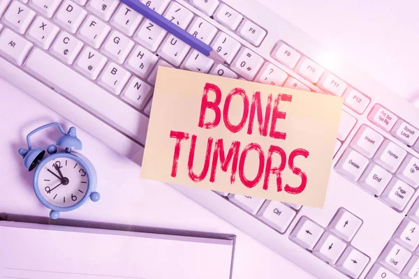 Conceptual hand writing showing Bone Tumors. Business photo text can be either benign or malignant growths found in the bone Flat lay above empty note paper on pc keyboard pencils and clock.