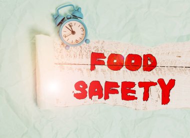 Conceptual hand writing showing Food Safety. Business photo text conditions and practices that preserve the quality of food Alarm clock and torn cardboard on a wooden classic table backdrop.