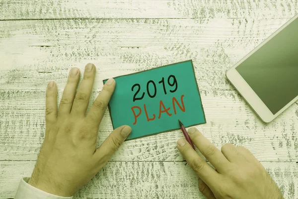 Conceptual hand writing showing 2019 Plan. Business photo text setting up your goals and plans for the current year or in 2019 Hand hold note paper near writing equipment and smartphone.