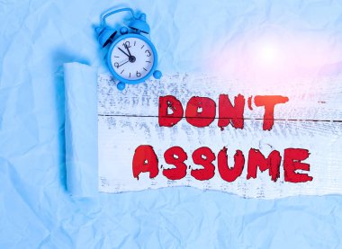 Don T varsayımını gösteren kavramsal el yazısı. İş fotoğrafı metni sorgusuz veya kanıtsız bir şeyin doğru olduğunu kabul etmez Alarm saati ve karton yırtılmış tahta bir masa arkaplanı.