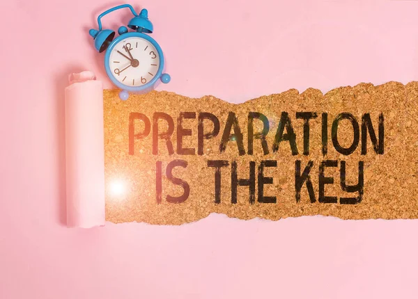 Text sign showing Preparation Is The Key. Conceptual photo it reduces errors and shortens the activities Alarm clock and torn cardboard placed above a wooden classic table backdrop.