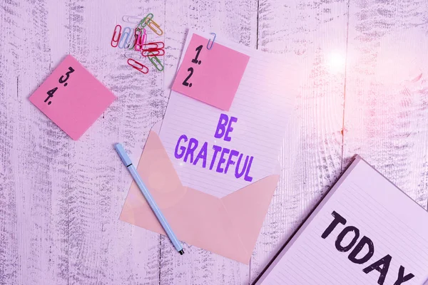 単語の執筆テキストは感謝しなさい。受信した何かのための感情や感謝を示すためのビジネスコンセプト封筒シート紙粘着ノートボールペンノートパッドクリップ木製の背景. — ストック写真