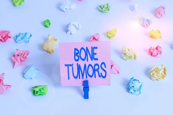 Writing note showing Bone Tumors. Business photo showcasing can be either benign or malignant growths found in the bone Colored crumpled paper empty reminder white floor clothespin.