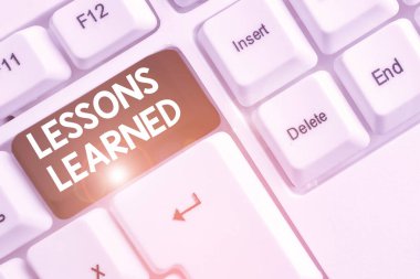 Ders Öğrenilmiş 'i gösteren bir not yazıyorum. Deneyimle elde edilen bilgi veya anlayışı gösteren iş fotoğrafı beyaz arkaplanın üzerinde nota kağıdıyla birlikte beyaz pc klavye.