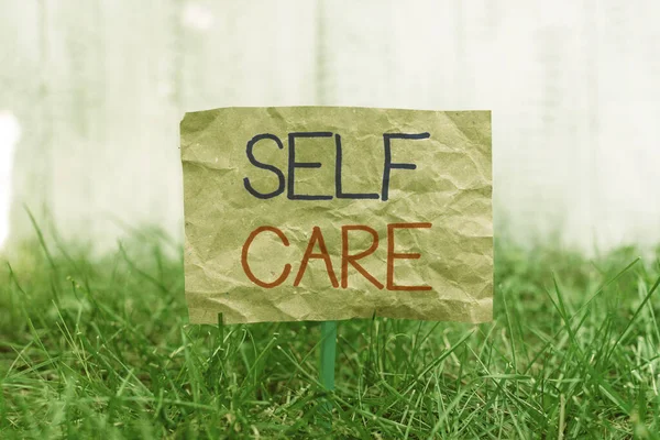 Word writing text Self Care. Business concept for the practice of taking action to improve one s is own health Crumpled paper attached to a stick and placed in the green grassy land. — Stock Photo, Image