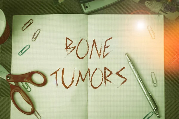 Text sign showing Bone Tumors. Conceptual photo can be either benign or malignant growths found in the bone Scissors and writing equipments plus math book above textured backdrop.