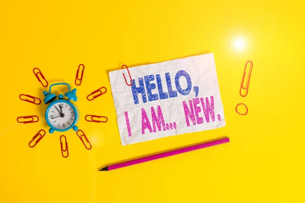 Handwriting text Hello I Am New. Concept meaning introducing oneself in a group as fresh worker or student Metal alarm clock clips crushed sheet pencil rubber band colored background.