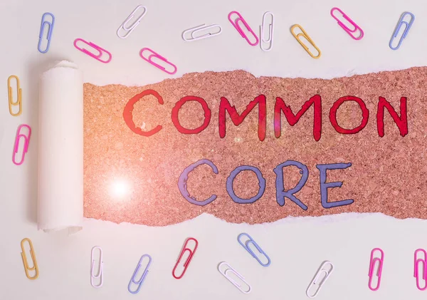 Kézírás szöveg Common Core. Koncepció jelentése halmaz akadémiai szabványok a matematika és az angol nyelv gemkapocs és szakadt karton fölött elhelyezett fa klasszikus asztal háttér. — Stock Fotó