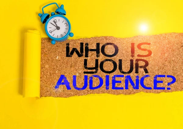 Handwriting text writing Who Is Your Audience Question. Concept meaning who is watching or listening to it Alarm clock and torn cardboard placed above a wooden classic table backdrop.