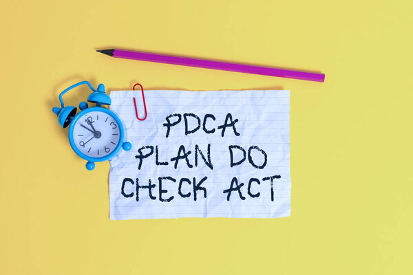 Conceptual hand writing showing Pdca Plan Do Check Act. Business photo showcasing Deming Wheel improved Process in Resolving Problems Metal alarm clock ccrushed sheet pencil colored background.