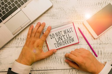 Writing note showing Do Not Wait Until Tomorrow. Business photo showcasing needed to do it right away Urgent Better do now Hand hold note paper near writing equipment and smartphone.