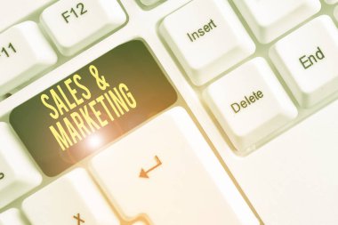 Conceptual hand writing showing Sales And Marketing. Business photo text Promotion Selling Distribution of Goods or Services White pc keyboard with note paper above the white background.