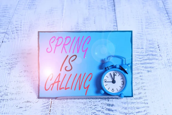 Conceptual hand writing showing Spring Is Calling. Business photo showcasing Time for flowers March coming beautiful colors Sunny Alarm clock tilted above buffer wire in front of notepaper. — Stock Photo, Image