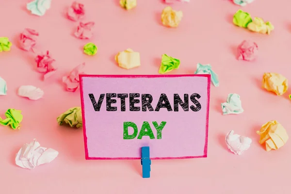 Writing note showing Veterans Day. Business photo showcasing a public holiday to honour US veterans and victims of all wars Colored crumpled papers empty reminder pink floor background clothespin.