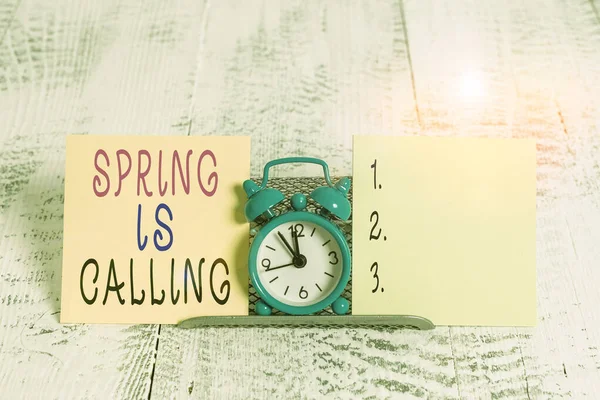 Writing note showing Spring Is Calling. Business photo showcasing Time for flowers March coming beautiful colors Sunny Mini blue alarm clock standing above buffer wire between two paper. — Stock Photo, Image