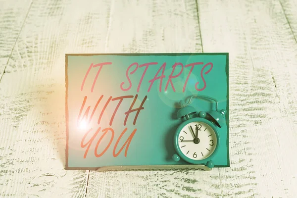Conceptual hand writing showing It Starts With You. Business photo showcasing Motivation for starting doing something Have discipline Alarm clock tilted above buffer wire in front of notepaper. — 图库照片