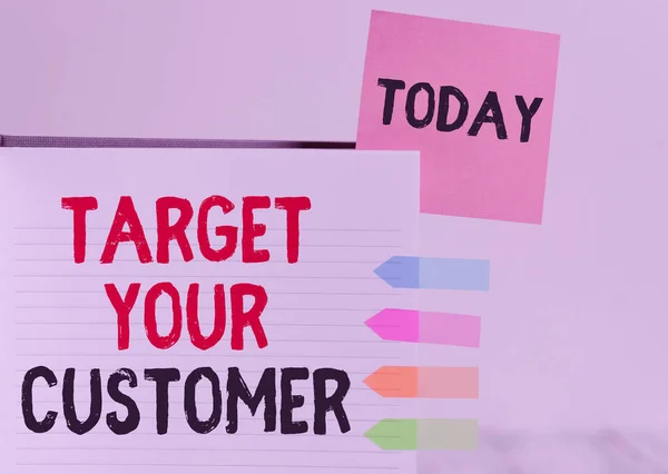 Word writing text Target Your Customer. Business concept for Tailor Marketing Pitch Defining Potential Consumers Hard cover note book sticky note arrow banners inserted clear background.