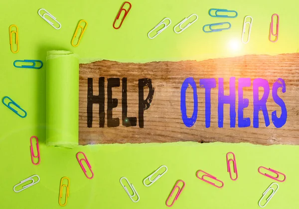 Text sign showing Help Others. Conceptual photo the action of helping someone to do something or assistance Paper clip and torn cardboard placed above a wooden classic table backdrop.
