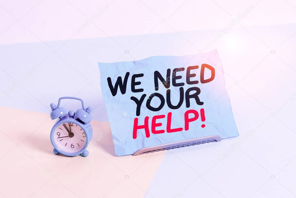 Writing note showing We Need Your Help. Business photo showcasing asking someone to stand with you against difficulty Alarm clock beside a Paper sheet placed on pastel backdrop.
