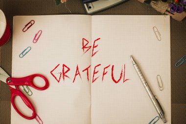 Text sign showing Be Grateful. Conceptual photo feeling or showing an appreciation for something received Scissors and writing equipments plus math book above textured backdrop.