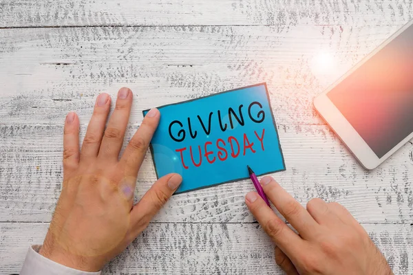 Conceptual hand writing showing Giving Tuesday. Business photo text international day of charitable giving Hashtag activism Hand hold note paper near writing equipment and smartphone.