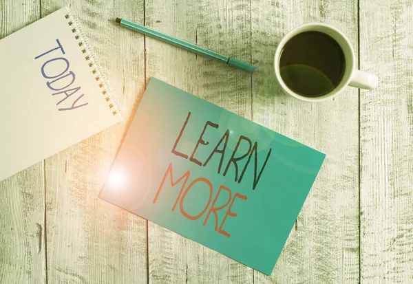 Nota de escritura que muestra Learn More. Foto de negocios mostrando el conocimiento o la habilidad adquirida por la instrucción Considerable aprendizaje Estacionario colocado junto a una taza de café negro sobre la mesa de madera . —  Fotos de Stock