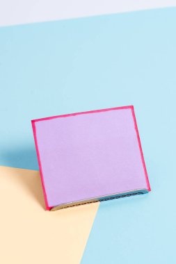 Paper sheet placed tilted on a buffer wire with a soft pastel backdrop. Notepaper on the edge of empty plain multi colours table. Artistic way of arranging flat lays photography