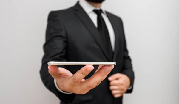 Man människa med skägg bära formella arbetskläder hålla högteknologiska smartphone-enhet. Man klädd i arbetskläder plus slips håller liten mobil hi tech telefon med en hand — Stockfoto