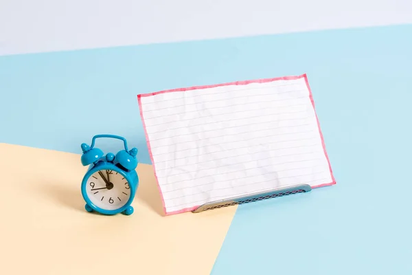 Mini kis méretű ébresztőóra mellett egy papírlap elhelyezett dönthető. Notepaper szélén üres sima, többszínű asztali háttér. Művészeti módja elrendezése lakás fekteti fotózás — Stock Fotó
