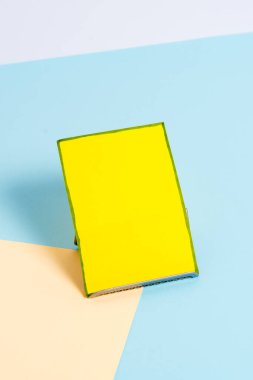 Paper sheet placed tilted on a buffer wire with a soft pastel backdrop. Notepaper on the edge of empty plain multi colours table. Artistic way of arranging flat lays photography