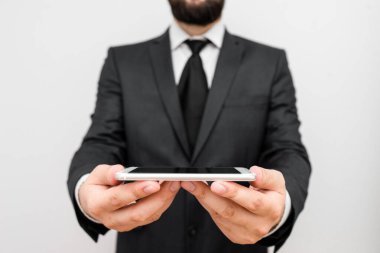 Sakallı bir erkek resmi iş kıyafetleri giyer yüksek teknoloji akıllı telefon cihazı taşır. İş elbisesi ve kravat takmış bir adam iki eliyle cep telefonu tutuyor.