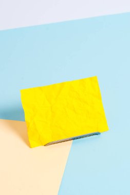 Paper sheet placed tilted on a buffer wire with a soft pastel backdrop. Notepaper on the edge of empty plain multi colours table. Artistic way of arranging flat lays photography