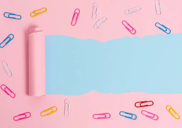Ripped cardboard with paper clip placed above a soft colour table. Thick torn paper and stationary on a pastel plain backdrop. Artistic way of arranging flat lays photography