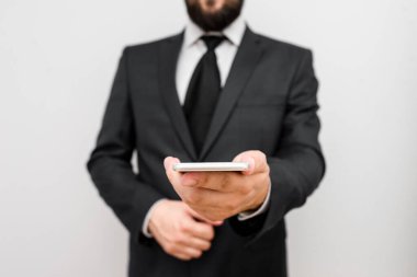 Sakallı bir erkek resmi iş kıyafetleri giyer yüksek teknoloji akıllı telefon cihazı taşır. İş elbisesi giymiş bir adam ve kravatlı küçük cep telefonlu bir adam tek elini kullanıyor.