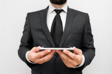 Sakallı bir erkek resmi iş kıyafetleri giyer yüksek teknoloji akıllı telefon cihazı taşır. İş elbisesi ve kravat takmış bir adam iki eliyle cep telefonu tutuyor.