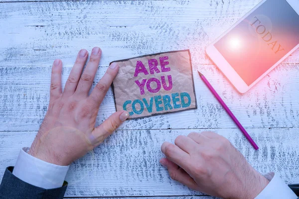 Textskylt med texten Are You Covered. Konceptuell bild Fråga om hur läkemedel omfattas av din plan Hand hålla anteckning papper nära skrivutrustning och modern smartphone-enhet. — Stockfoto