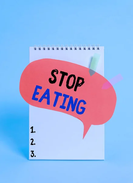 Text sign showing Stop Eating. Conceptual photo cease the activity of putting or taking food into the mouth Spiral notepad speech bubble arrow banners lying cool pastel background.