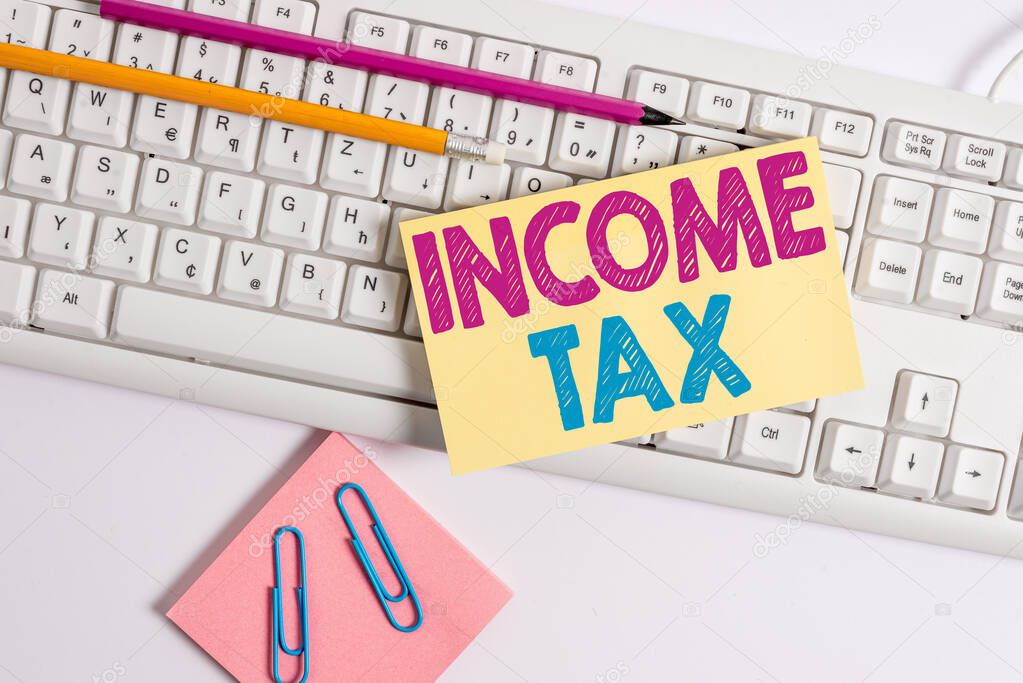 Conceptual hand writing showing Income Tax. Business photo showcasing Annual charge levied on both earned and unearned income White keyboard with note paper and clips on white background.