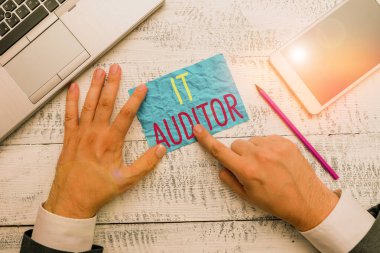 It Auditor 'u gösteren kavramsal el yazısı. Sistemin denetlenmesine ve doğrulanmasına yetki veren iş fotoğrafı metni. Yazma ekipmanı ve akıllı telefon yanındaki el yazısı kağıdı tutulur..