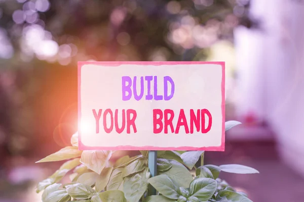 여러분의 브랜드를 만드는 것을 보여 주는 문자 표지판. 개념적 인 사진을 만들어 상업적 정체 성 마케팅 광고 일반빈 종이 막대기에 부착하고 녹색 잎 식물에 배치. — 스톡 사진