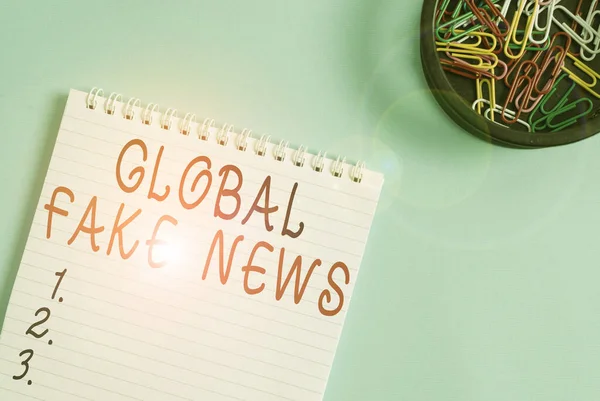 Escribiendo nota mostrando Global Fake News. Exposición de fotos de negocios Información falsa Periodismo Mentiras Desinformación Engaño Cuaderno vacío en blanco y estacionario colocado sobre fondo de color pastel . — Foto de Stock