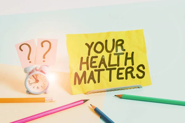 Znak tekstowy pokazujący Twoje zdrowie ma znaczenie. Koncepcyjne zdjęcie dobre zdrowie jest najważniejsze między innymi Mini rozmiar budzika obok stacjonarnego umieszczone przechylone na pastelowym tle. — Zdjęcie stockowe