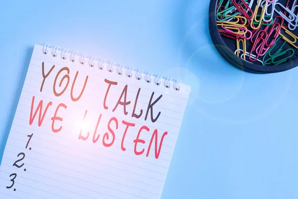 Writing note showing You Talk We Listen. Business photo showcasing Two Way Communication Motivational Conversation Blank empty notebook and stationary placed above pastel colour backdrop.