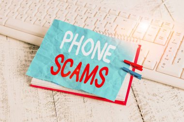Kelime yazma telefon dolandırıcılığı. Yasadışı para elde etmek için telekomünikasyon kullanımı konsepti. Kağıt defteri hatırlatması. Mandallı çarşaf, beyaz klavye ışığı ahşap..