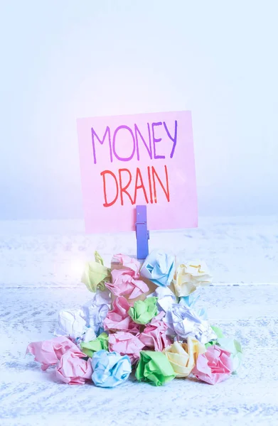 Writing note showing Money Drain. Business photo showcasing To waste or squander money Spend money foolishly or carelessly Reminder pile colored crumpled paper clothespin wooden space.