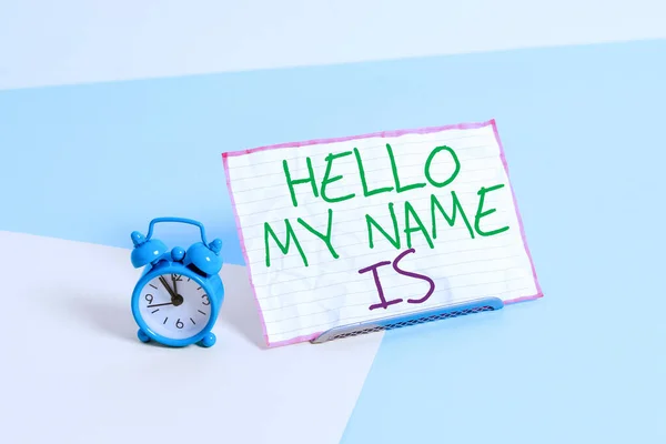 Kézírás szövegírás Hello My Name Is. Koncepció azt jelenti, hogy bemutatkozik az új bemutató munkavállalók, mint a bemutató Mini méretű ébresztőóra mellett egy papír lap billentett pasztell háttér. — Stock Fotó