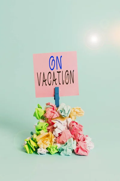 Text sign showing On Vacation. Conceptual photo period spent away from home or business in travel or recreation Reminder pile colored crumpled paper clothespin reminder blue background. — Stock Photo, Image
