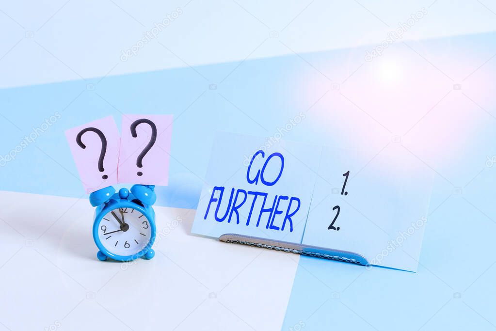 Writing note showing Go Further. Business photo showcasing To make a bolder statement about something being discussed Alarm clock beside a Paper sheet placed on pastel backdrop.